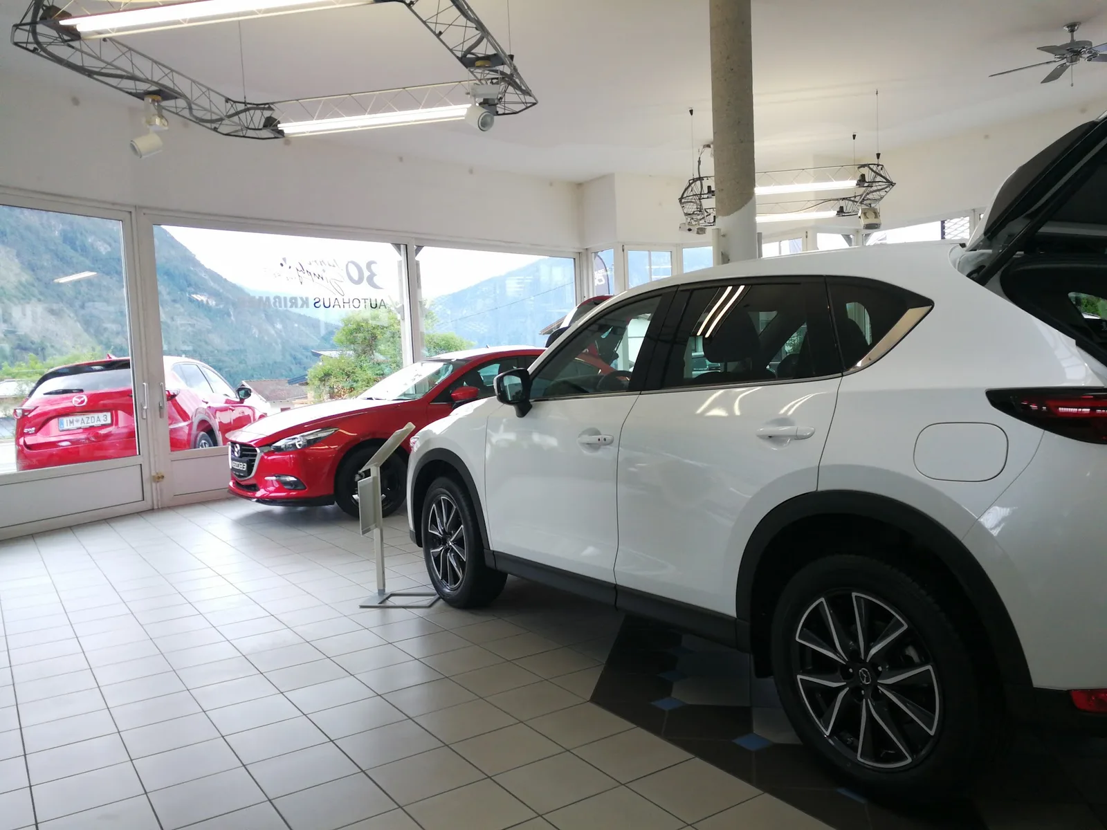 Blick in den Schauraum mit einem weißen Mazda CX-5 und einem roten Mazda 3