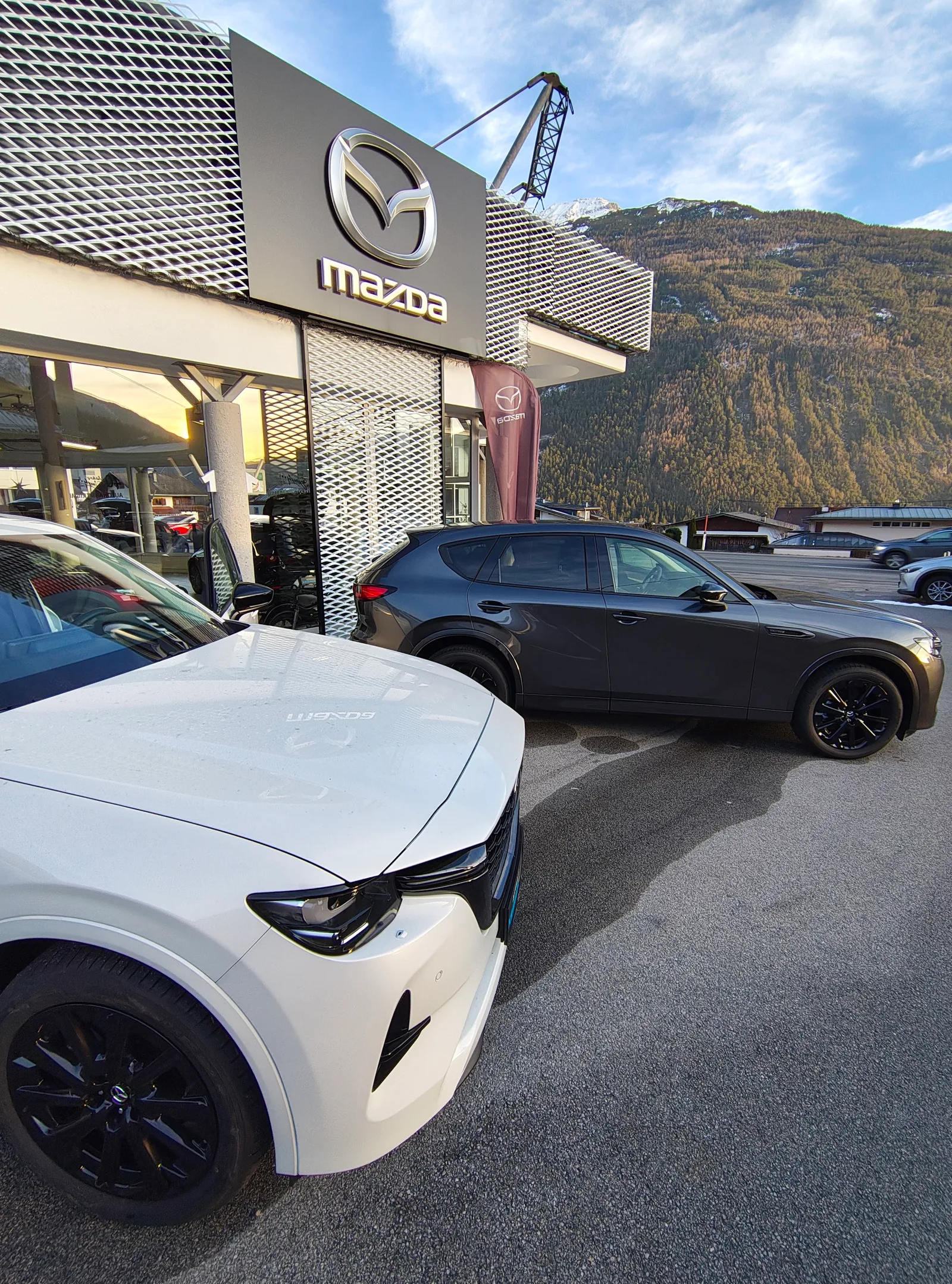 Der Mazda-Pylon vor dem Autohaus, dahinter die bewaldeten Hänge über Tarrenz