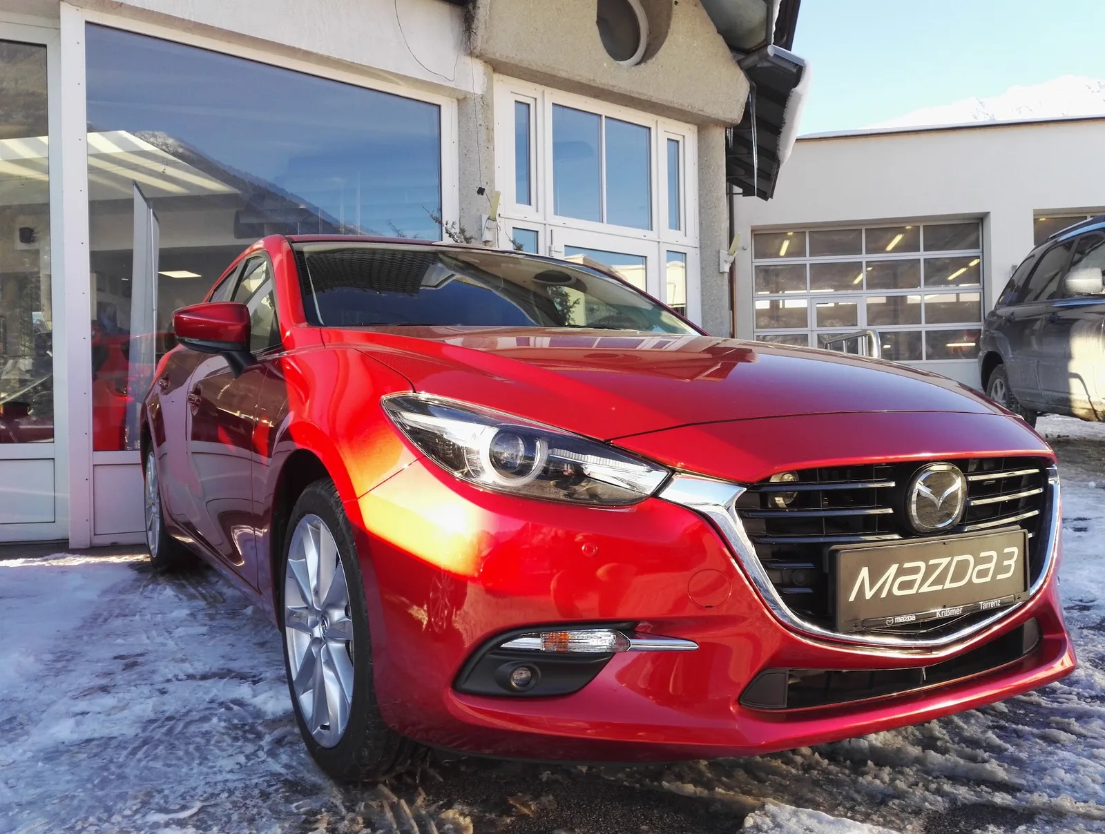 Ein roter Mazda 3 vor den Werkstatttoren des Autohauses im Schnee